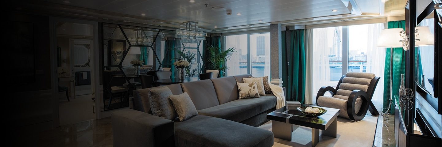 A luxury cruise suite sitting room with a sofa and floor-to-ceiling windows